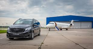 Schwarzer Van steht vor einem Hangar neben einem Privatjet.